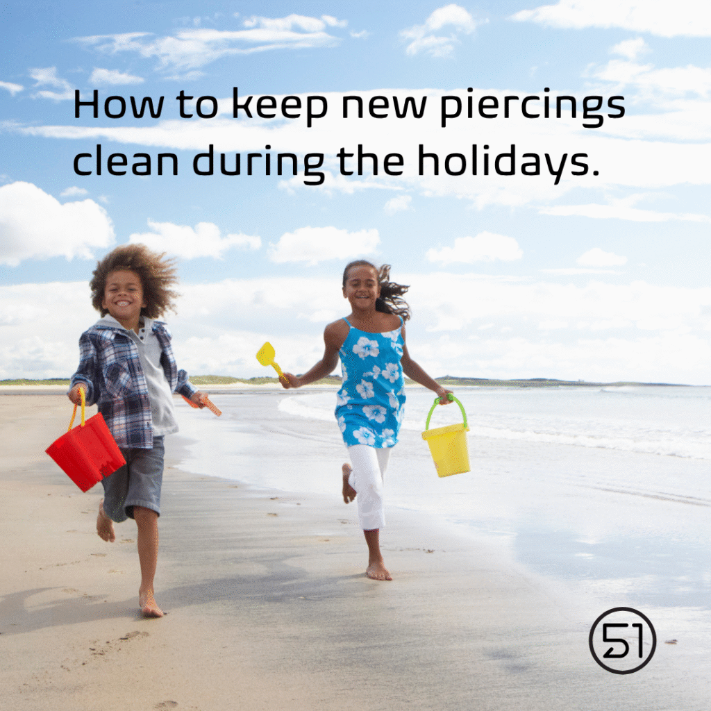 Image shows two children playing on the beach. Text reads "How to keep new piercings clean during the holidays"
